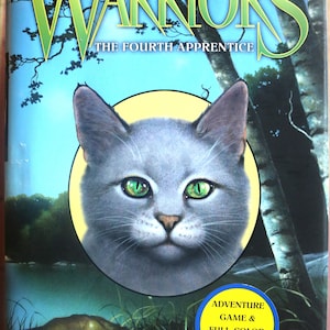 May include: Book cover for "Warriors: The Fourth Apprentice" by Erin Hunter. The cover features a gray cat with green eyes in front of a lake and trees. The title is in large, green letters. A yellow sticker advertises an adventure game and a full-color map.