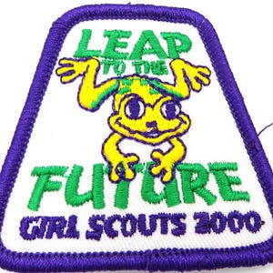 May include: Embroidered patch with a white background, a purple border, and a cartoon frog. The patch reads "LEAP TO THE FUTURE GIRL SCOUTS 2000" in green and purple thread. The frog is yellow with green accents.