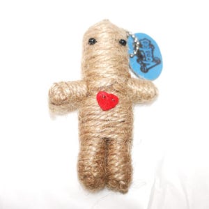 May include: A handmade voodoo doll crafted from natural twine, featuring a red heart and black bead eyes. A blue tag with the text "Voo Doo" is attached. The doll has a simple, stylized human form.