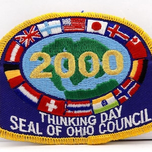 May include: A blue patch with a gold embroidered border. The patch features the number "2000" in gold, a green earth graphic, and flags of various countries. Text at the bottom reads "Thinking Day Seal of Ohio Council."
