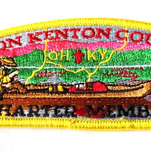 May include: Embroidered patch with a yellow border featuring a canoe scene. The patch reads "Simon Kenton Council" and "Charter Member." The design includes a person in a canoe, mountains, and the letters "OH KY."