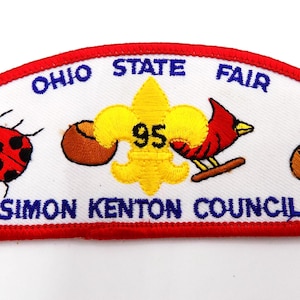 May include: Embroidered patch with a red border and white background. The patch features the text "OHIO STATE FAIR" and "SIMON KENTON COUNCIL". It includes a ladybug, a fleur-de-lis with the number 95, a cardinal, and a brown object.