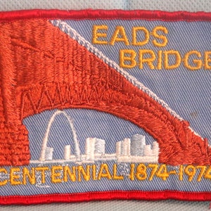 May include: A blue and red embroidered patch with the text "Eads Bridge Centennial 1874-1974" and a depiction of the St. Louis Arch.