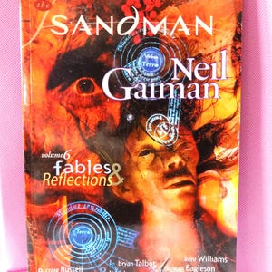 May include: The Sandman: Fables & Reflections, volume 6, by Neil Gaiman. The cover features a surreal illustration with a face and eye, set against a fiery orange and brown background. The book is a fully remastered edition.
