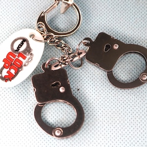 May include: A silver keychain with a white oval charm that says "Lock Up Your Fun" and two silver handcuffs.
