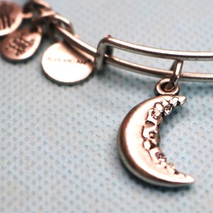 May include: Silver charm bracelet with a crescent moon charm. The moon charm has a detailed design of flowers and leaves.