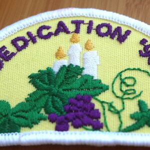May include: Purple embroidered patch with white stitching around the edges. The patch is yellow with a design of three white candles, green leaves, and purple grapes. The text "REDEDICATION 1995-1996" is embroidered in purple around the edge of the patch.