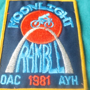 May include: A blue and white embroidered patch with the text "Moonlight Ramble DAC 1981 AYH" and a red circle with a bicycle silhouette.