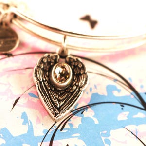 May include: A silver charm bracelet with a heart-shaped charm featuring a pair of angel wings and a clear crystal in the centre.