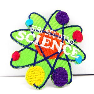 May include: A green embroidered patch in the shape of an atom, with the word "SCIENCE" in white letters. The atom has a blue outline and colorful dots in red, yellow, purple, and blue. The text "GIRL SCOUTS OF" is above the word "SCIENCE".