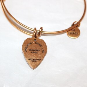 May include: Gold charm bracelet with a gold charm that reads "Direction - Divine Aid - Guardian Angel" and "Alex and Ani &copy; 2017". The bracelet also has a small gold charm that reads "Energy".