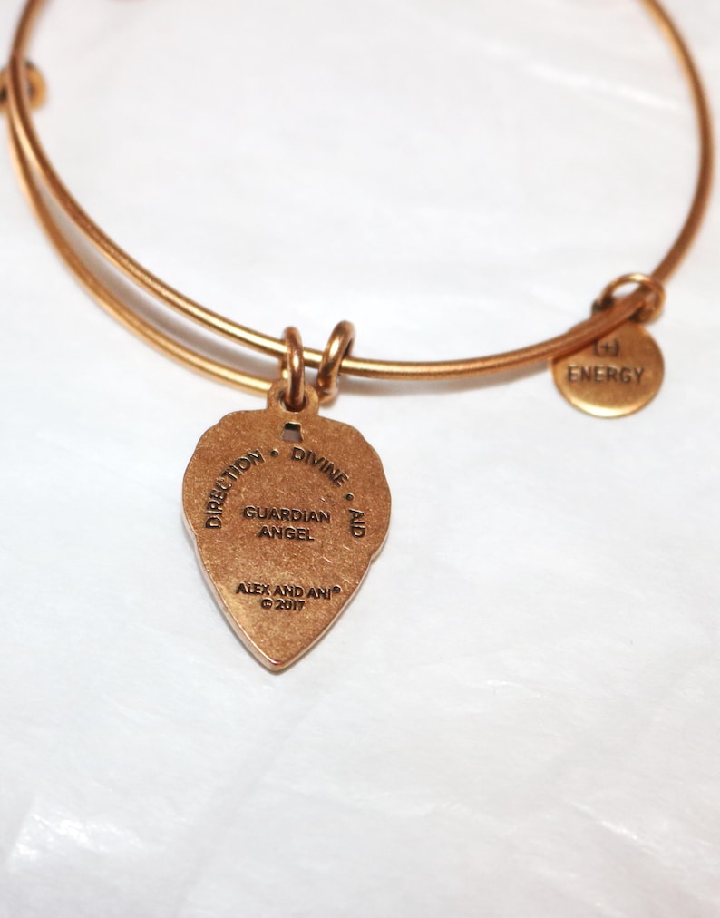 May include: Gold charm bracelet with a gold charm that reads "Direction - Divine Aid - Guardian Angel" and "Alex and Ani &copy; 2017". The bracelet also has a small gold charm that reads "Energy".