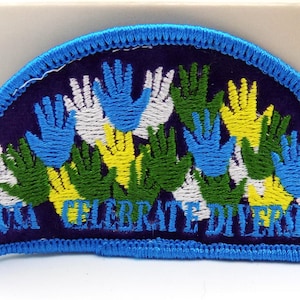 May include: A half-circle patch with a blue border and a dark blue background. The patch features multiple handprints in white, blue, green, and yellow. The text "CELEBRATE DIVERSITY" is embroidered in yellow.