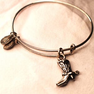 May include: A silver charm bracelet with a silver boot charm. The bracelet is made of two thin bands of metal.