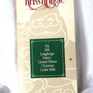 May include: A vintage Longaberger Pottery Christmas Cookie Mold box. The box is cream-colored with a Santa Claus illustration and the words "Kriss Kringle" in burgundy. A green label reads "The 1991 Longaberger Pottery Limited Edition Christmas Cookie Mold."