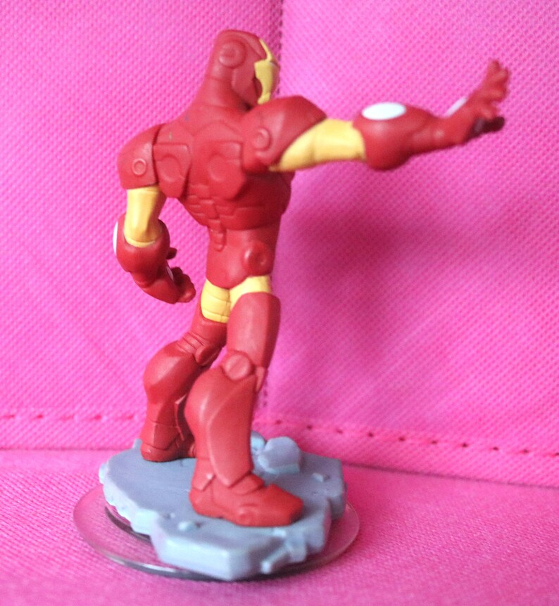 May include: A red and yellow Iron Man action figure, posed with one arm extended. The figure is on a grey base with a clear plastic disc. The figure's armour is red with yellow accents on the arms, legs, and head.