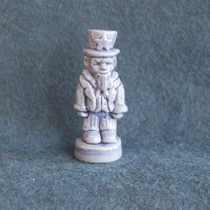 May include: A blue ceramic figurine of Uncle Sam wearing a hat with a star on it. He is wearing a blue coat and pants and has a white beard.