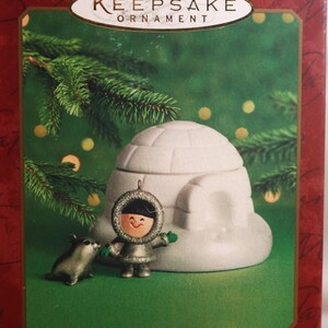 May include: Hallmark Keepsake Ornament set of two, featuring a white igloo and a small silver figurine of a person in a winter coat standing next to a silver animal. The box reads "Frosty Friends" and "Decorations des Fetes".