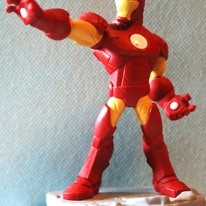 May include: Red and yellow Iron Man action figure with a gray base. The figure is posed with one arm outstretched and the other hand holding a repulsor beam.