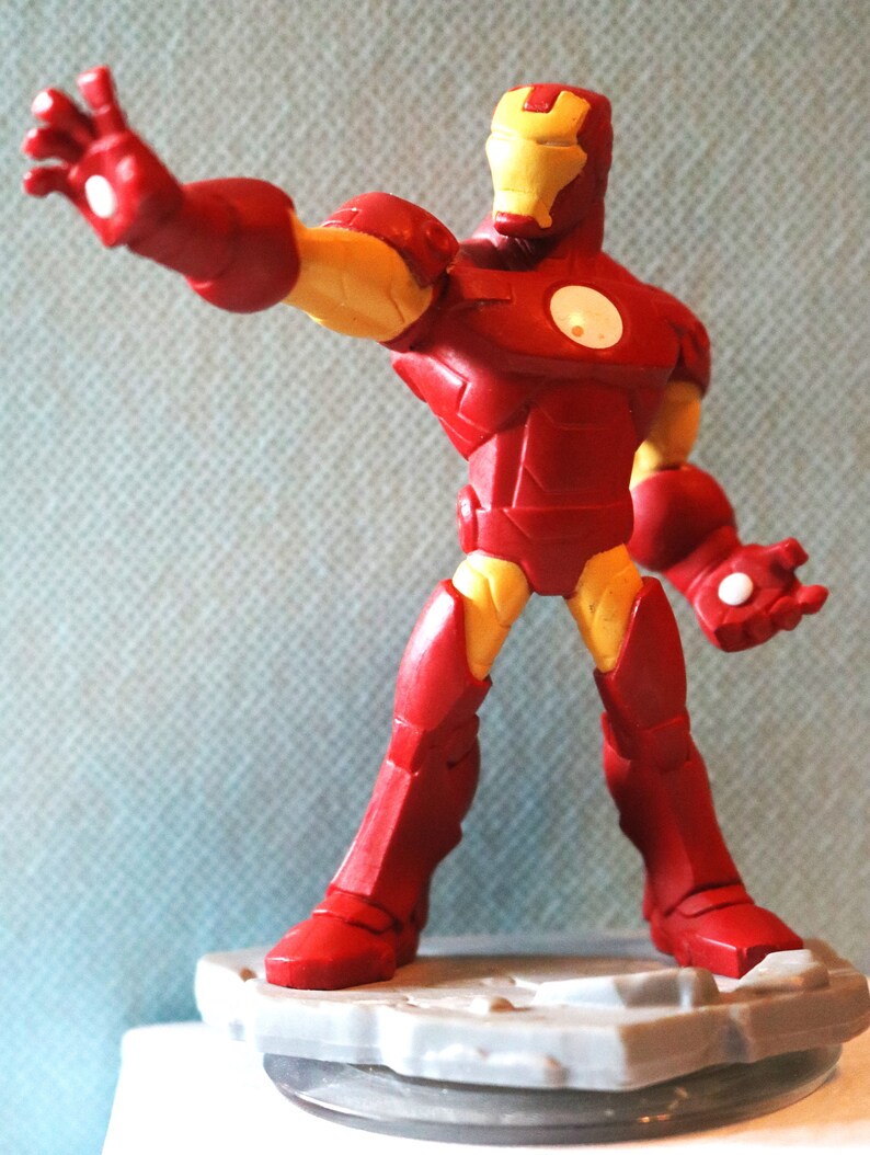 May include: Red and yellow Iron Man action figure with a gray base. The figure is posed with one arm outstretched and the other hand holding a repulsor beam.