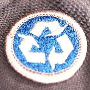 May include: A blue and white embroidered patch with a recycling symbol. The symbol is made up of three arrows that form a circle.
