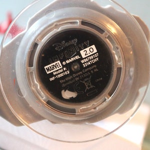 May include: Close-up of the bottom of a Disney Infinity 2.0 Marvel figure. The figure is black with white text that reads "Disney Infinity 2.0", "MARVEL", "Model #:", "INF-1000102", "W86799107", "3314TCHY", "The Walt Disney Company", "(Benelux) BV 213215 9 NL", and "China".