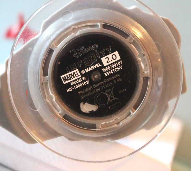 May include: Close-up of the bottom of a Disney Infinity 2.0 Marvel figure. The figure is black with white text that reads "Disney Infinity 2.0", "MARVEL", "Model #:", "INF-1000102", "W86799107", "3314TCHY", "The Walt Disney Company", "(Benelux) BV 213215 9 NL", and "China".