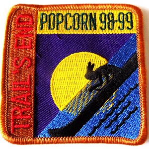 Puede incluir: Parche bordado con el texto "TRAILS END" a la izquierda y "POPCORN 98-99" en la parte superior. El parche presenta un sol amarillo, una silueta negra de un conejo e imágenes de montañas azules y moradas.