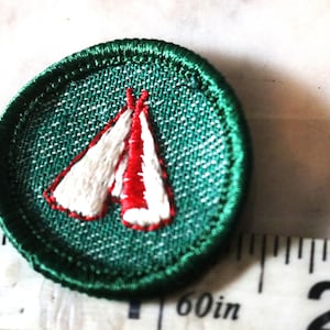 May include: Green embroidered patch with a white and red tent design. The patch is about 1.5 inches in diameter.