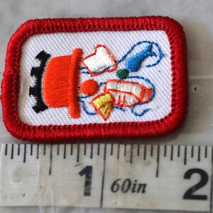 May include: A red, white, and blue embroidered patch with a red fire hydrant and a variety of colorful objects coming out of the top. The patch is about 1 inch wide.