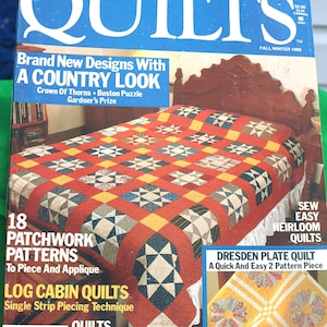 May include: A vintage copy of "Country Quilts" magazine. The cover features a patchwork quilt with red, blue, yellow, and white squares. Text includes "Brand New Designs With A Country Look" and "18 Patchwork Patterns".