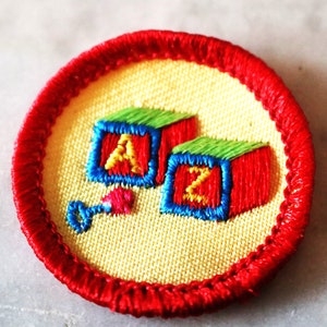 May include: A red, white, and blue embroidered patch with the letters A and Z on blocks. The patch is surrounded by a red border.