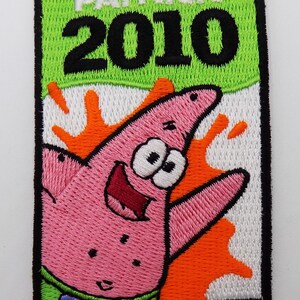 May include: Embroidered patch featuring Patrick Star from Spongebob Squarepants. The patch has a pink starfish design with a smiling face, set against an orange and white background. The text "PATRICK 2010" is displayed at the top in white and black.