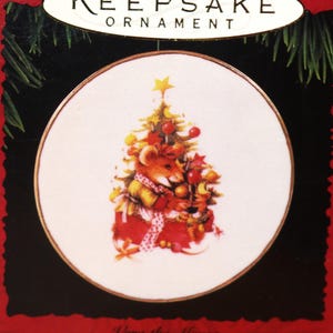 May include: A white porcelain plate with a gold rim features a Christmas tree with a mouse holding a red ornament. The text "Vera the Mouse" and "Collector's Plate - Display Stand Included" is printed below the image.