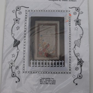 May include: A white cross-stitch pattern with a white picket fence border. The pattern features a bird with red and yellow feathers, flowers, and the text "What lies behind us and what lies before us are tiny matters compared to what lies within us".