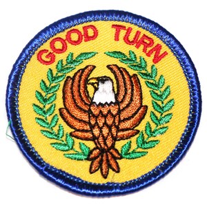 May include: Embroidered patch with a yellow background, blue border, and the words "GOOD TURN" in red. The patch features a brown eagle with a white head and a green laurel wreath.