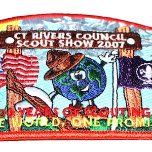 May include: A colorful embroidered patch with the text "CT Rivers Council Scout Show 2007" and "100 Years of Scouting One World, One Promise". The patch features an American flag, a purple flag with a fleur-de-lis, and a cartoon Earth holding a sign.