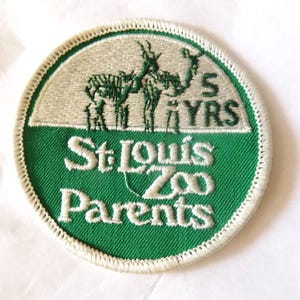 May include: A circular patch with a green and white design. The top half features two green animal figures and the text "5 YRS". The bottom half reads "St. Louis Zoo Parents" in white lettering, with a white border.