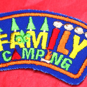 May include: A blue embroidered patch with orange, yellow, green, and red stitching. The patch says "FAMILY CAMPING" with a stylized tree design.
