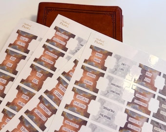 May include: Bible tabs with a watercolor design in shades of brown, orange, and gray. The tabs are labeled with book names and the word "PEARL" is printed at the top. A brown leather Bible is in the background.