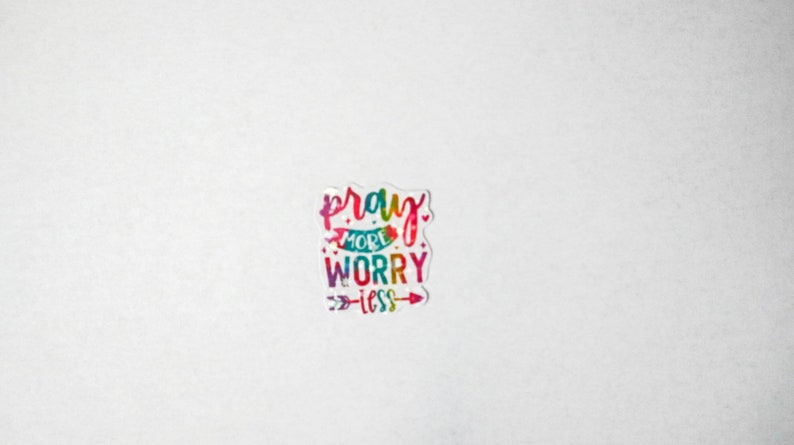 May include: A colorful sticker with the text "pray more worry less" in a rainbow font with an arrow pointing to the right.