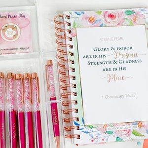 Könnte beinhalten: Ein Schreibwarenset mit Stiften und einem Planer. Die Stifte haben ein rosa-klares Kristall-Design mit roségoldenen Akzenten. Der Planer hat florale Designs und den Text "Glory & Honor are in His Presence".
