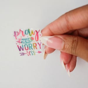 May include: A colorful sticker with the text "pray more worry less" in a rainbow font. The sticker has a white background and a rainbow arrow pointing to the right.