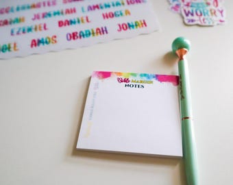May include: A notepad with a watercolor design and the text "Bablo Maker Notes" on the front. A teal pen with a gold top is next to the notepad.
