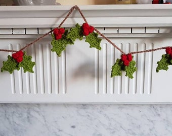May include: A green and red crocheted holly garland with red berries hangs on a white mantel.