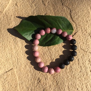 May include: A bracelet made of pink and black beads. The pink beads are made of rose quartz and the black beads are made of lava rock.