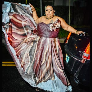 Peut inclure: Robe bustier aux tons bordeaux, marron et cr&egrave;me, avec une jupe fluide. La robe est orn&eacute;e d'un motif floral et est port&eacute;e &agrave; l'ext&eacute;rieur pr&egrave;s d'une voiture noire. Le tissu semble l&eacute;ger et a&eacute;r&eacute;.