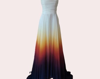 May include: A white strapless gown with a gradient ombre design. The skirt transitions from white to yellow, orange, red, and finally dark blue at the hem.