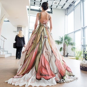Peut inclure: Une longue robe fluide avec un motif floral aux tons de rose, vert et blanc. La robe a un dos nu et une longue tra&icirc;ne. La robe est adapt&eacute;e &agrave; une occasion sp&eacute;ciale, comme un mariage.