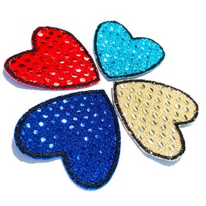 May include: Four heart-shaped patches with a sparkly, sequined design. The patches are red, blue, gold, and light blue.